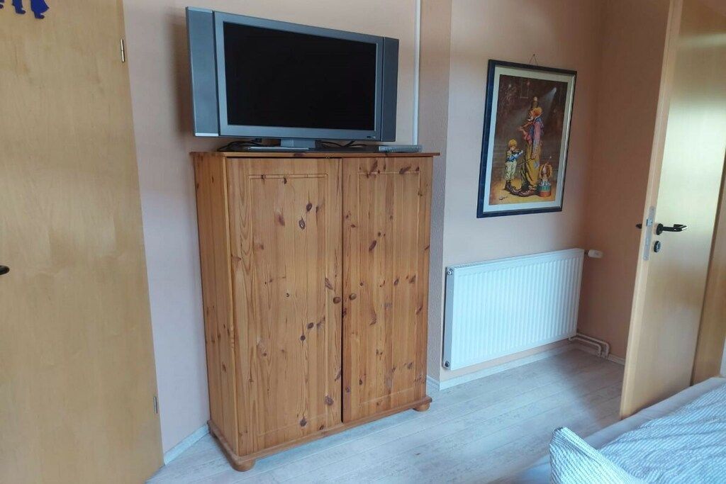 Une pièce avec une armoire en bois, un téléviseur posé sur le dessus, un radiateur et une porte.