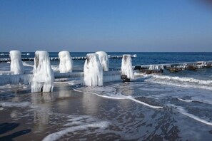 A beach with ice formations and a pier extending into the water. - Holiday home with 2 bedrooms (Kühlungsborn)