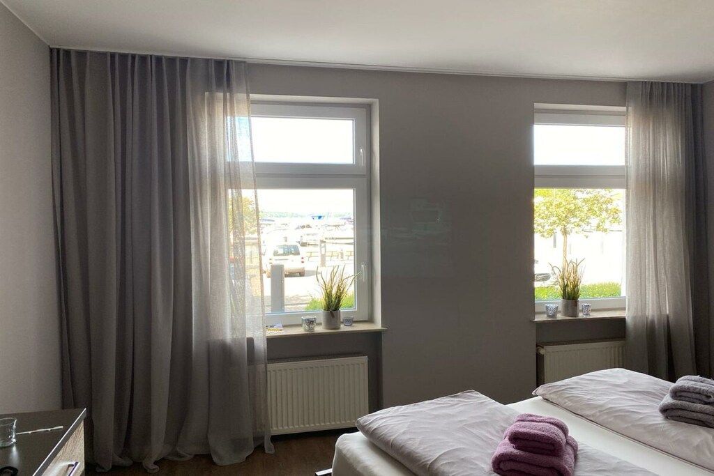 A hotel room with two beds, a radiator, a window with curtains, and a view of the outside.