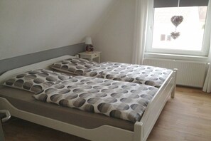Ein Einzelbett mit gemustertem Bettbezug und Kissen, ein Nachttisch mit Lampe sowie ein Fenster mit Dekoration.