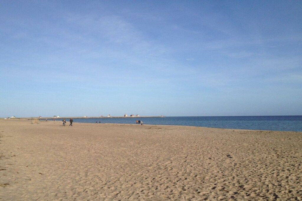 A wide sandy beach with a clear sky and calm sea.