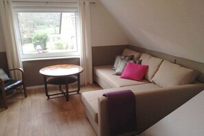 Ein gemütliches Zimmer mit einer Couch, einem kleinen runden Tisch und einem Fenster mit Vorhängen.