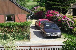 Ein Wohnhaus mit befestigter Auffahrt, ein rotes Auto auf der Auffahrt und ein schwarzes Auto vor dem Haus.
