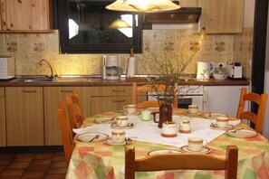 A kitchen with wooden cabinets, a window above the sink, and a dining table set with plates, cups, and a vase. - Holiday home with 1 bedroom (Jade2 Sehestedt)