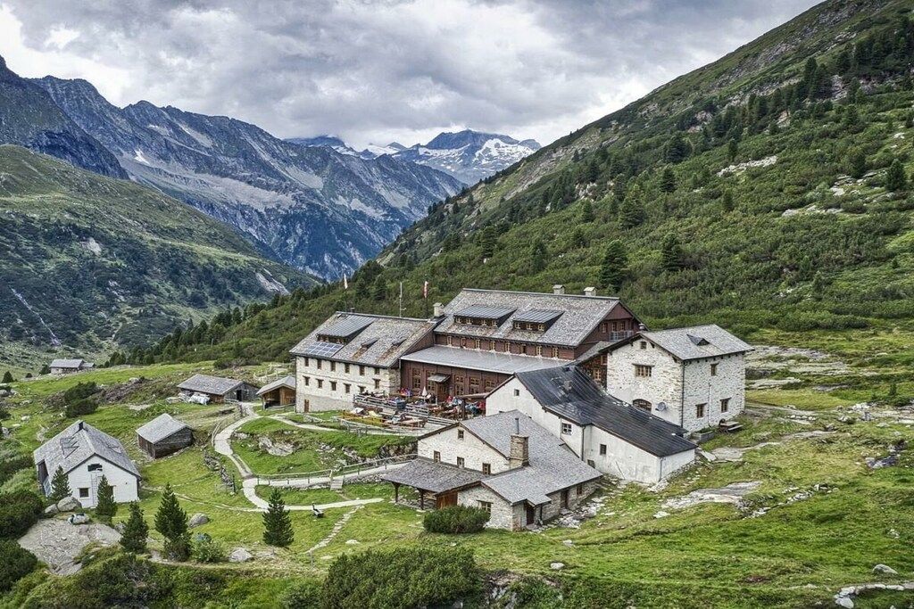 A traditional mountain lodge with multiple buildings, surrounded by lush greenery and mountains.