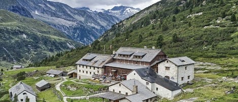 En traditionell fjällstuga med flera byggnader, omgiven av frodig grönska och berg.