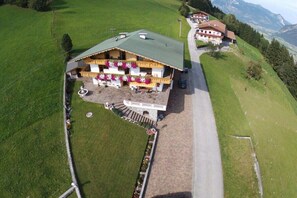 A two-story building with a green roof, a balcony with flower boxes, and a paved driveway leading to the entrance. - Holiday apartment with 2 bedrooms (Fügenberg)