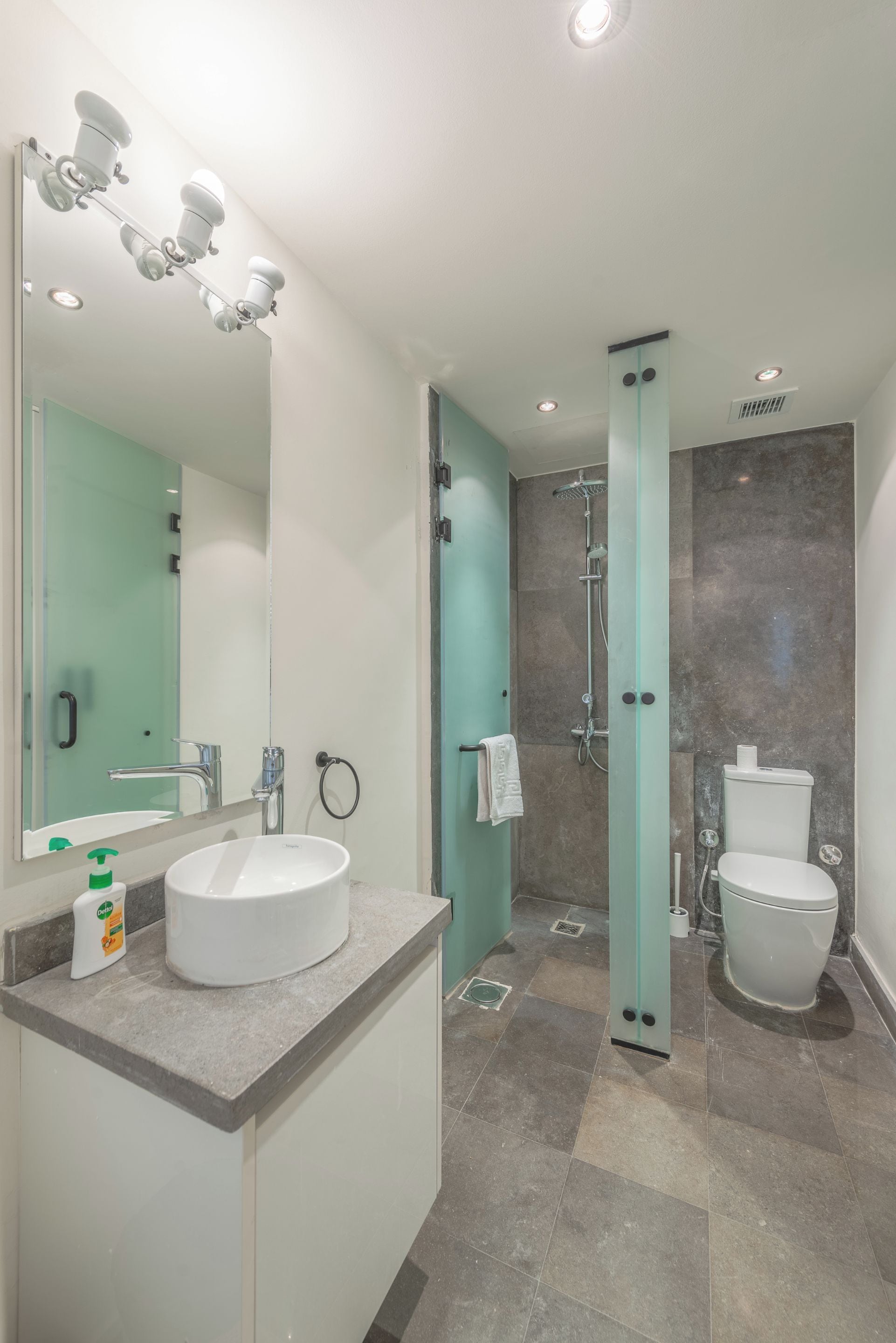 A modern bathroom with a large mirror, a sink, a shower, and a toilet.