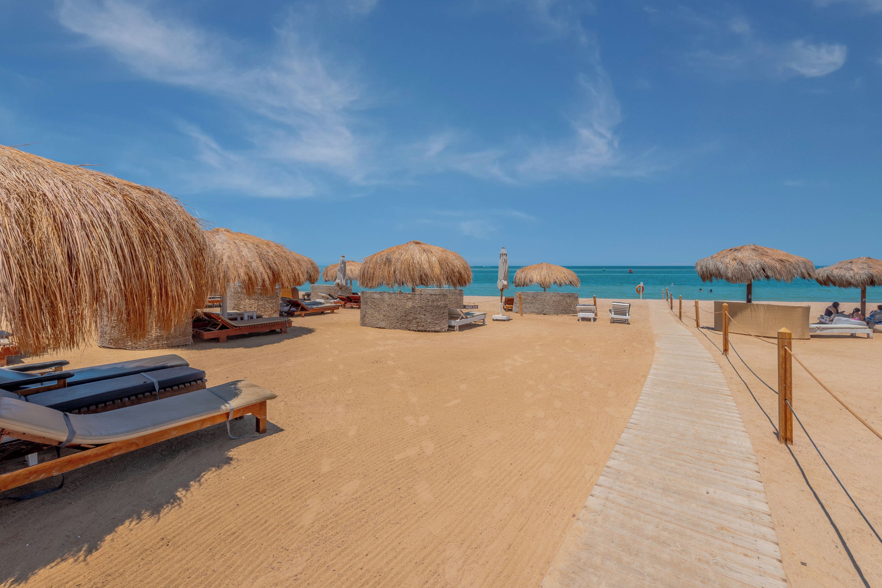 A beach with thatched umbrellas, lounge chairs, and a wooden walkway.