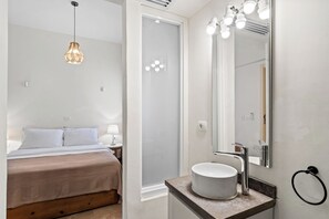 Et hotelværelse med seng, natbord, lampe og et badeværelse med vask, spejl og lys.