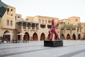 En gårdhave med en moderne skulptur, udendørs møbler og en bygning med buede vinduer og altaner.