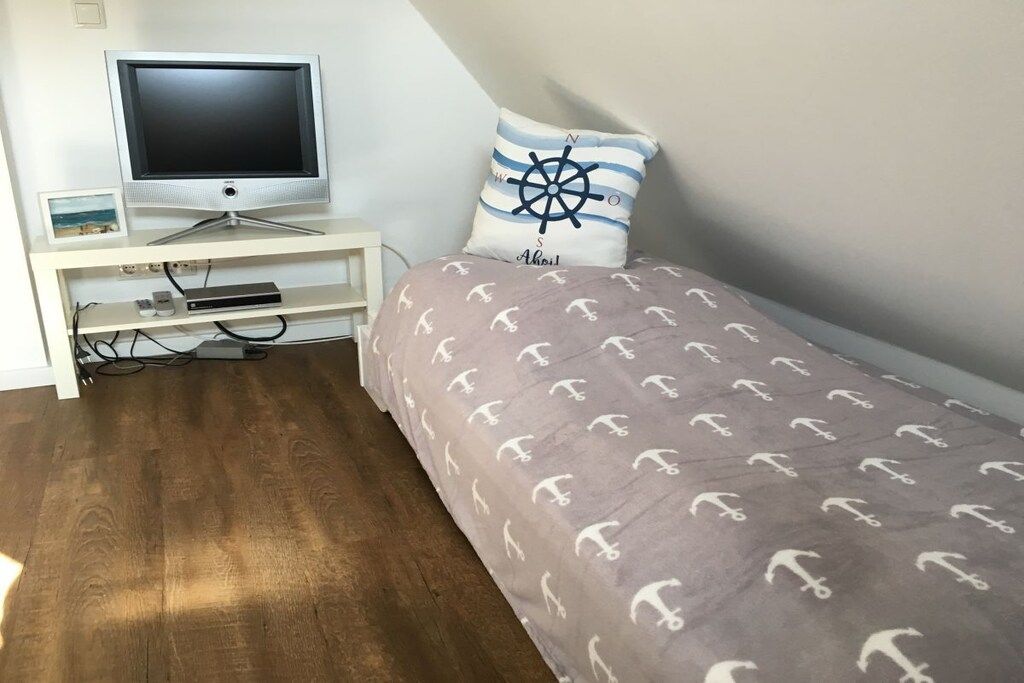 Een slaapkamer met een bed, een televisie op een standaard en een klein bureau met een fotolijst.