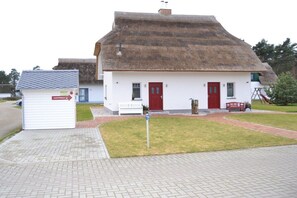 A white building with a thatched roof, a red door, and a small white bench outside. - (Zirchow)