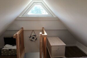 A room with a sloped ceiling, a skylight, a wooden crib, a small chest of drawers, and a life preserver decoration. - (Zirchow)