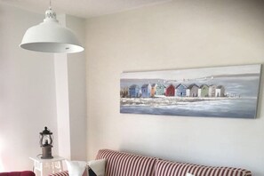 A room with a white lamp, a striped sofa, and a painting of colorful houses by the sea. - (Zirchow)