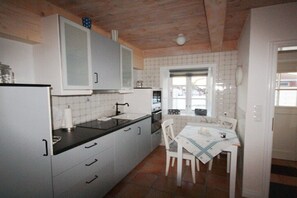 Een kleine keuken met witte kastjes, een zwart aanrechtblad en een eethoek met een tafel en stoelen.
