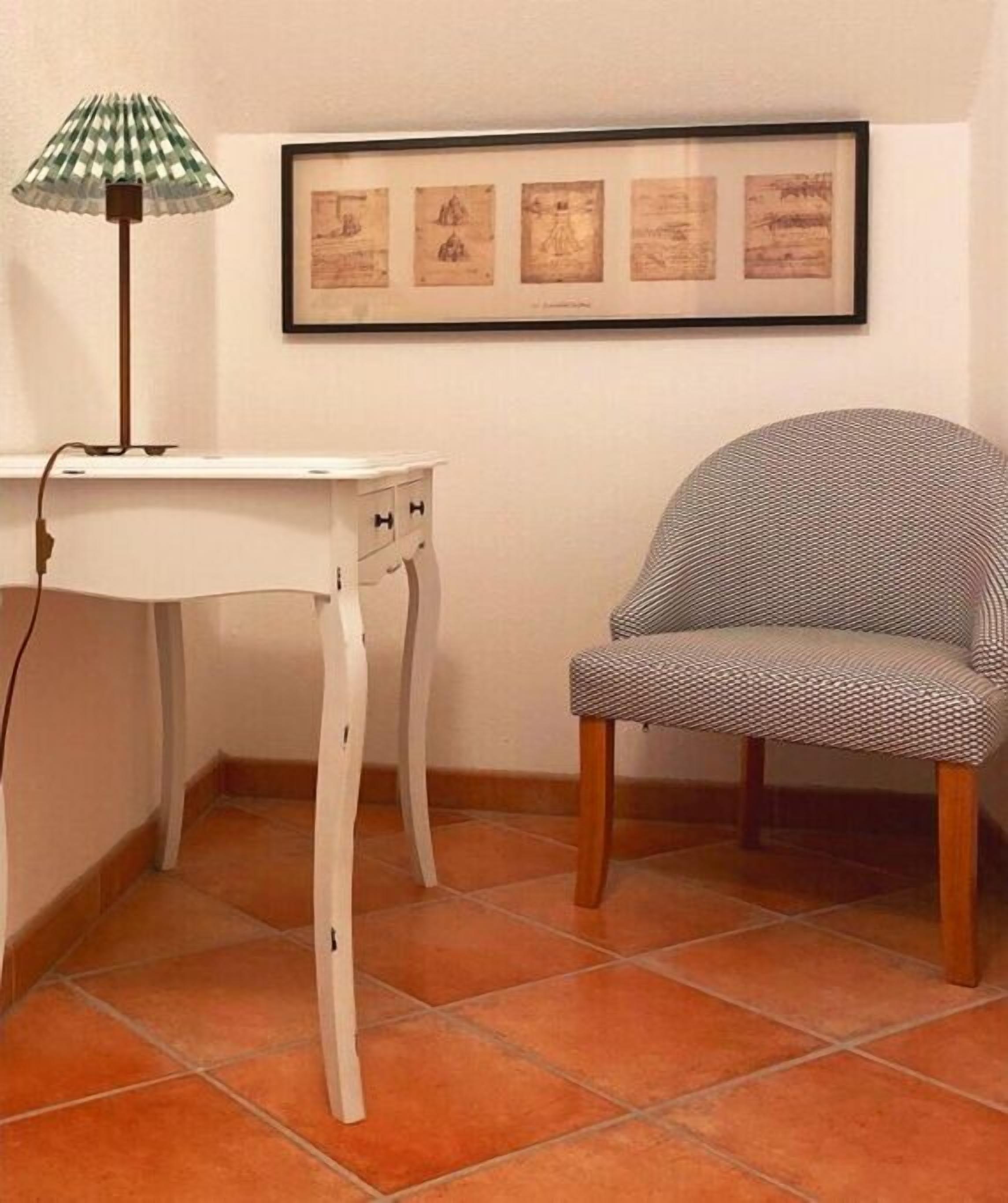 Une pièce d’angle avec une table blanche, une chaise à motifs, une lampe et un tableau encadré au mur.