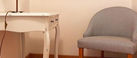 A corner room with a white table, a patterned chair, a lamp, and a framed picture on the wall.