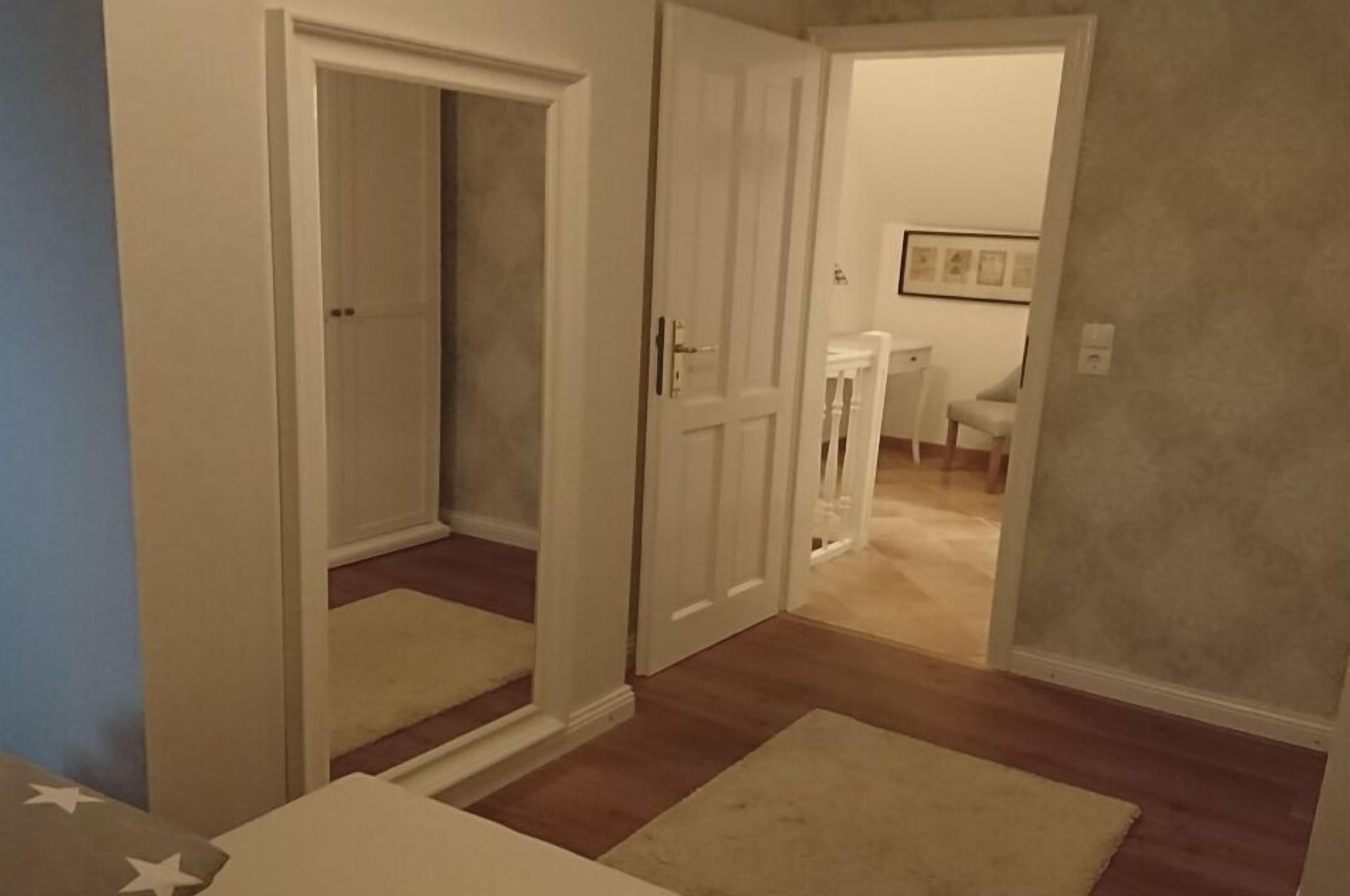 Habitació amb sòl de fusta, una porta blanca i una cadira blanca al fons.