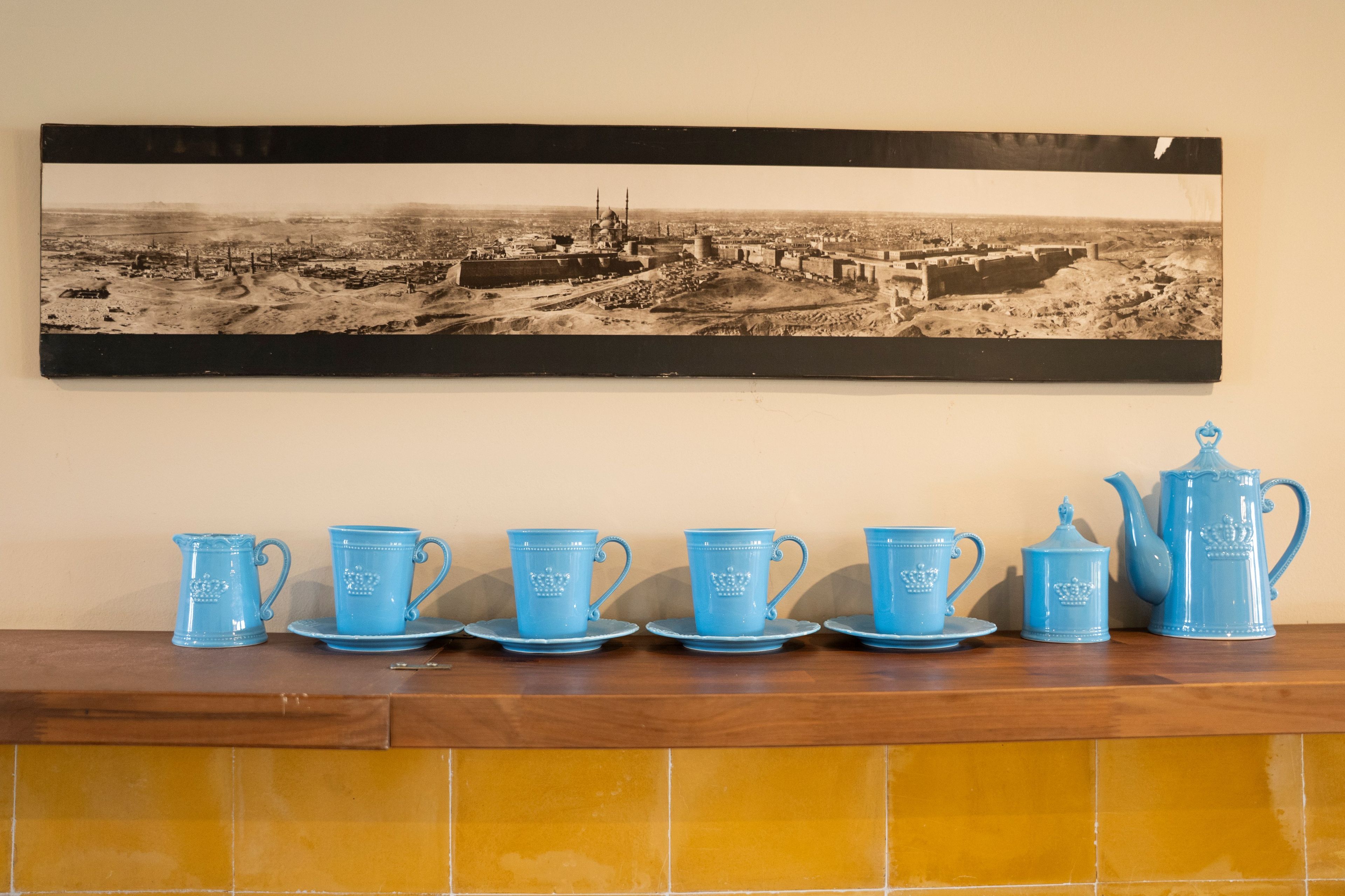Una colección de vajillas de té azules sobre un estante de madera, con una fotografía blanco y negro de un edificio histórico en la parte superior.