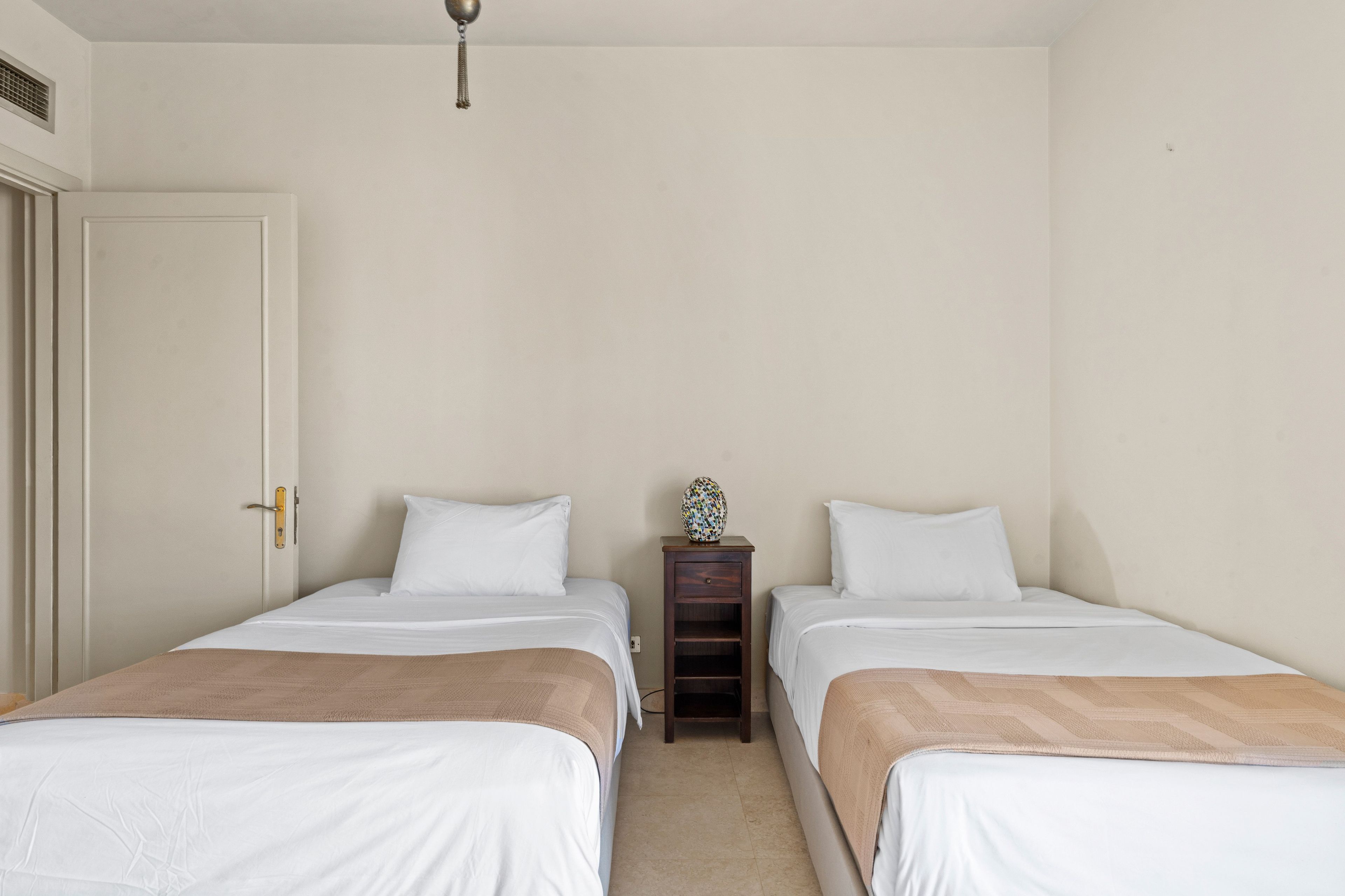 Una habitación sencilla y limpia con dos camas, una mesita de noche y una puerta.