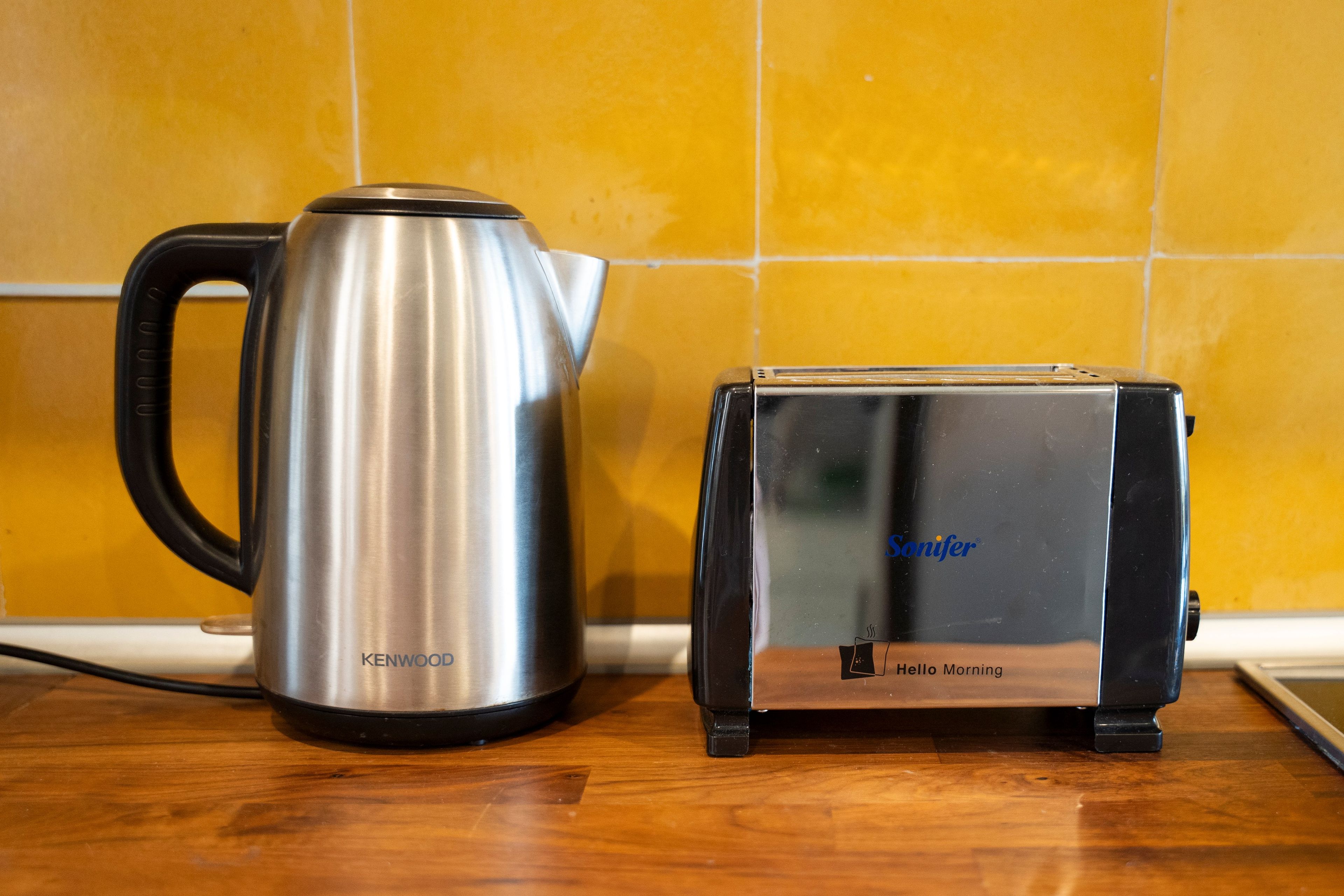 A stainless steel Kenwood kettle and a black Sonifer toaster on a wooden countertop.