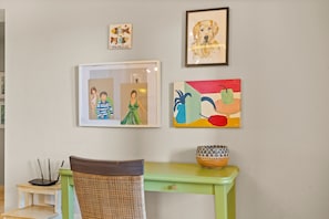 A room with a green table, a wicker chair, and various framed artworks on the wall. - New Marina View Apartment El Gouna (El Gouna)