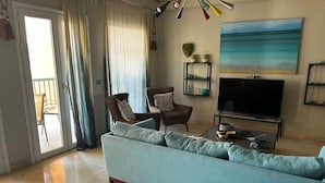 Sala de estar com sofá, cadeiras, televisão e um quadro na parede.