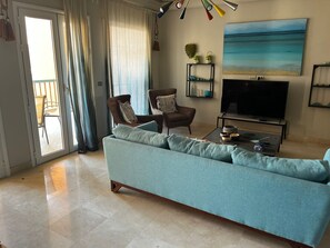 A living room with a sofa, chairs, a TV, and a painting on the wall. - Modern Apartment with Marina View (El Gouna)