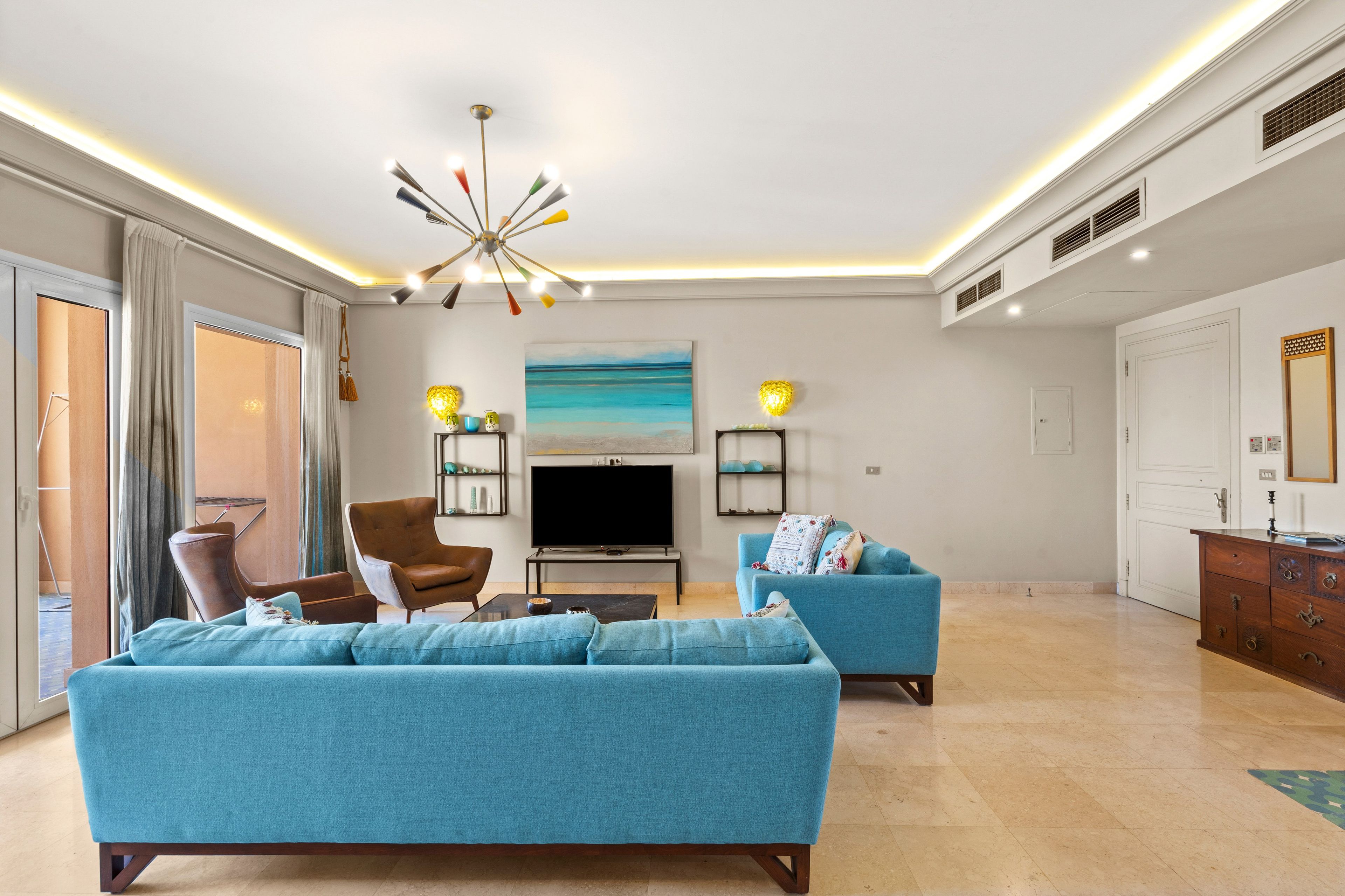 A spacious living room with a large sofa, a television, and a modern ceiling light fixture.