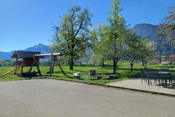 Un’area giochi con altalene e scivolo, tavoli da picnic e una piccola struttura in legno.