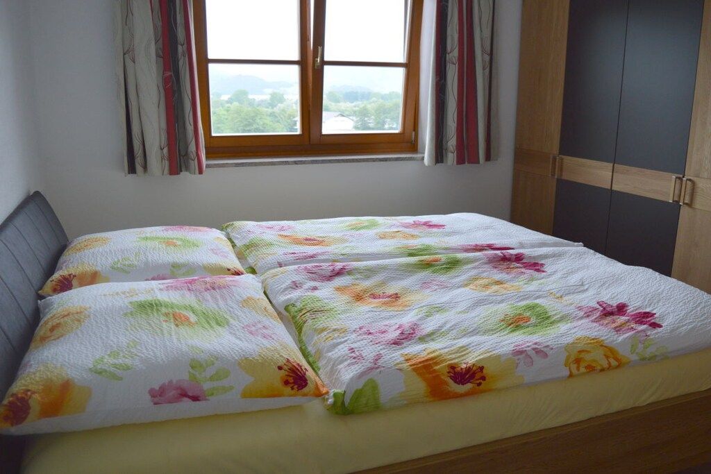 Un lit avec une literie à motifs floraux, une fenêtre avec des rideaux et une armoire.