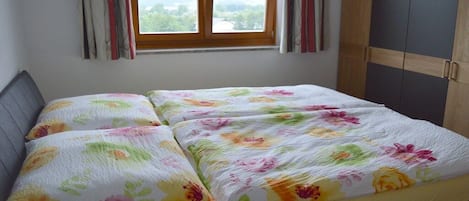 A bed with floral bedding, a window with curtains, and a wardrobe.