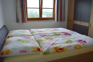 Ein Bett mit Blumenmuster auf der Bettwäsche, ein Fenster mit Vorhängen und ein Kleiderschrank.