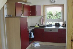A compact kitchen with red cabinets, a built-in oven, and a window providing natural light. - Small Forester's Lodge Pelzkuhl (Wesenberg OT Pelzkuhl)