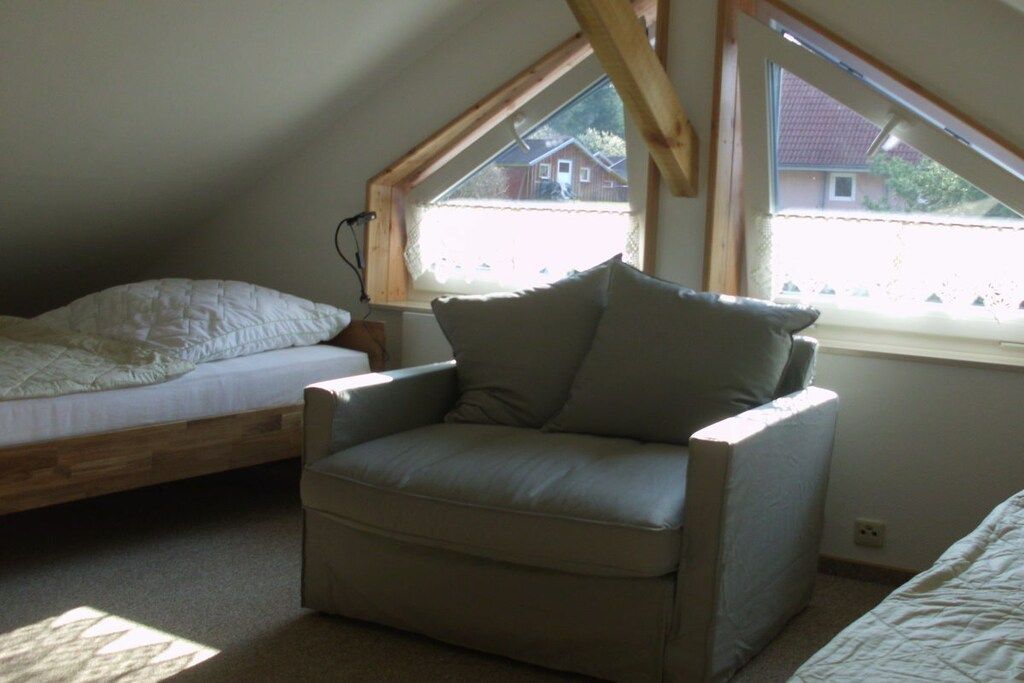Un dormitorio con cama rústica, una silla individual y ventana con vista a casas.