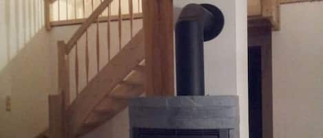 A wood-burning stove in a room with a wooden staircase and a white wall.