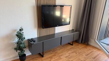 Ein modernes Wohnzimmer mit einem an der Wand montierten Flachbildfernseher, einem grauen Konsolentisch, einer Topfpflanze und Holzböden.
