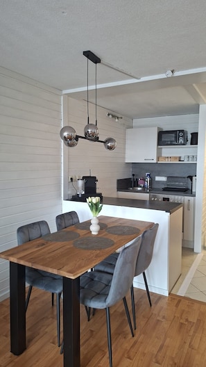 Una cocina moderna con una isla central, una mesa de comedor con sillas y una lámpara colgante.