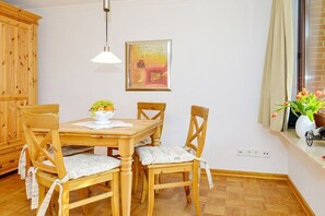 Ein Essbereich mit einem Holztisch und Stühlen, einer Hängelampe, einem gerahmten Bild an der Wand und einem Fenster mit Vorhängen.