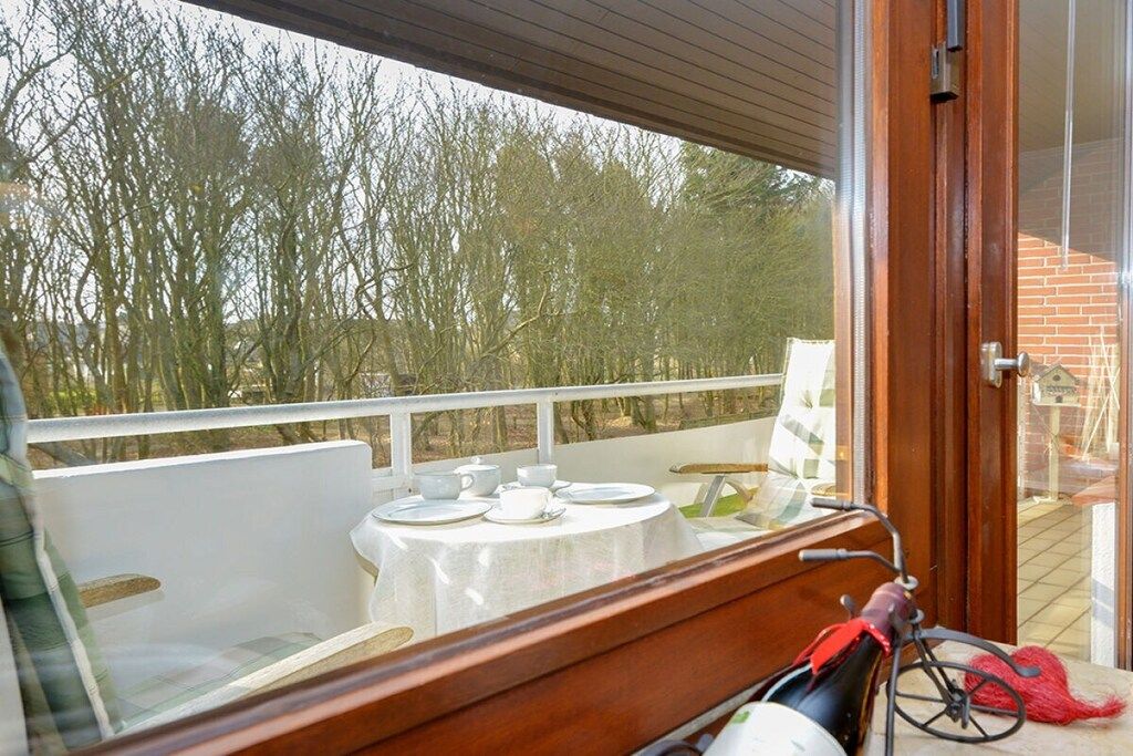 En balkon med et bord dækket til the, en cykel og udsigt til træer.