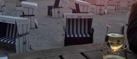 A beachside view with beach chairs numbered 939, 932, and 931, and a wooden table with a glass of white wine.
