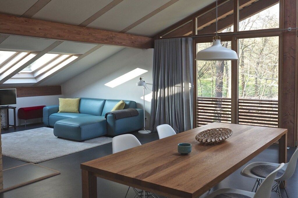 A modern living room with a wooden dining table, blue sofa, and large windows.