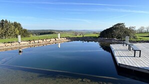 A tranquil outdoor pool area with a wooden deck and benches, surrounded by a stone wall and lush greenery.
