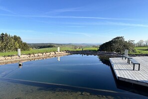 A tranquil outdoor pool area with a wooden deck and benches, surrounded by a stone wall and lush greenery.