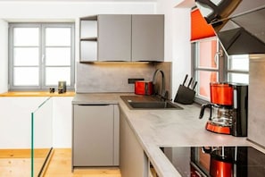 A modern kitchen with a built-in dishwasher, a coffee maker, and a window with blinds.