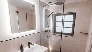 A modern bathroom with a glass-enclosed shower, a white sink, and a large mirror.