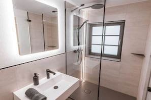 A modern bathroom with a glass-enclosed shower, a white sink, and a large mirror.