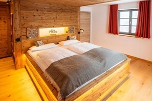 A wooden-framed bed with a headboard, a bedside table, and a window with red curtains.