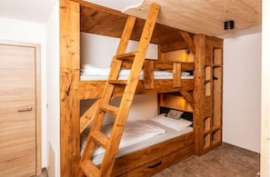 A bunk bed with a wooden ladder, a small drawer, and a headboard with a light fixture.